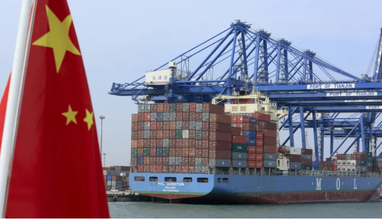 A Chinese flag flies on a vessel moving past shipping containers being unloaded at a Tianjin Port Group
