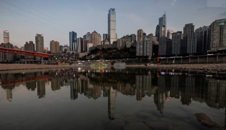 A file photo showing the city skyline is reflected in a pool left on the dry riverbed of the receding Jialing river, a tributary of the Yangtze, that is approaching record-low water levels during a regional drought in Chongqing, China, August 20, 2022. REUTERS